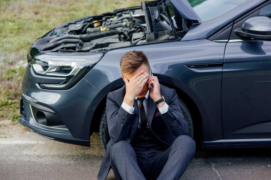car issues, upset man sat on road beside car with bonnet propped open