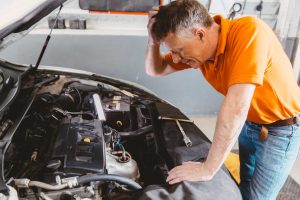 if your car fails its mot, frustrated mechanic looking at car with open bonnet