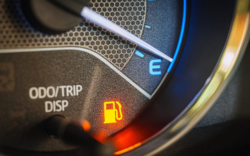 Car dashboard fuel gauge showing near empty with low fuel warning light illuminated