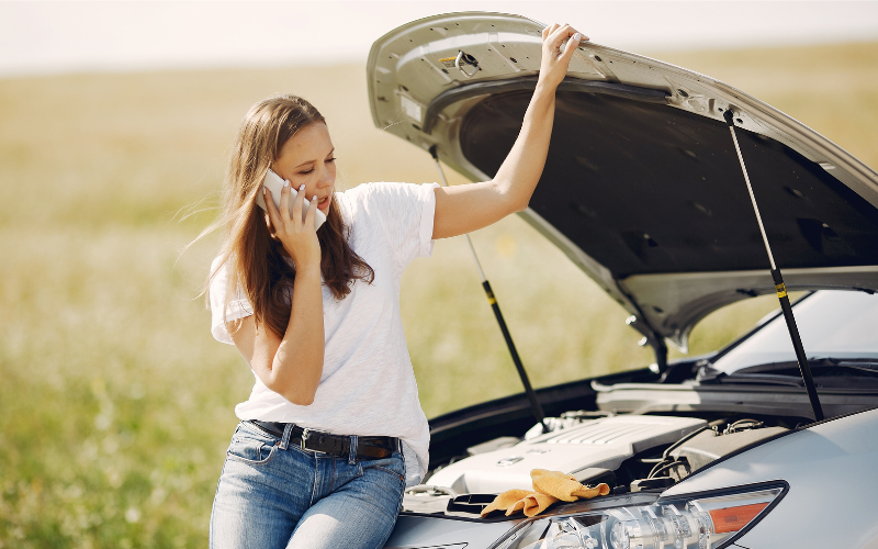 Driver standing beside broken down car with bonnet open during hot weather