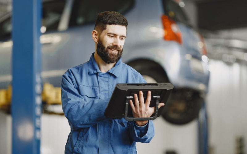 Vehicle technician using professional diagnostic equipment to inspect a customer's car in a workshop.