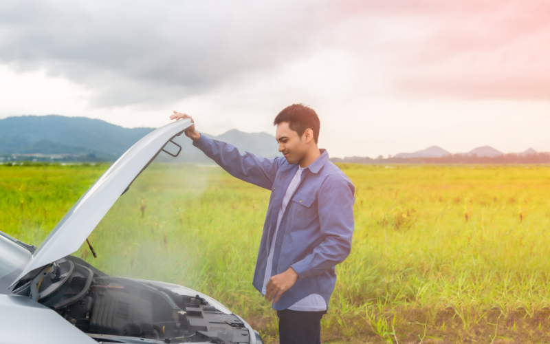 Driver checking an overheating car engine with steam coming from under the bonnet